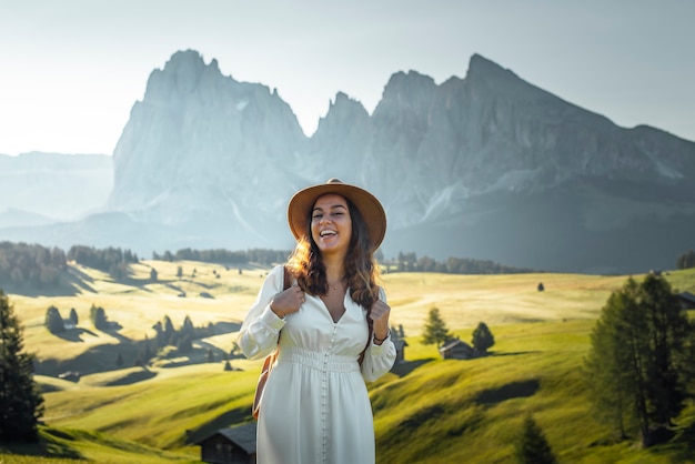 Heureuse jeune fille avec chapeau de robe blanche et sac à dos à Alpe di Siusi Dolomites