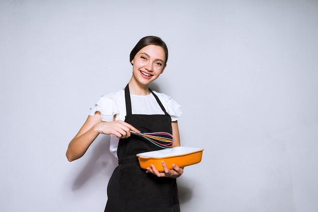 Heureuse jeune fille cuisinier dans un tablier noir préparant un délicieux gâteau, souriant