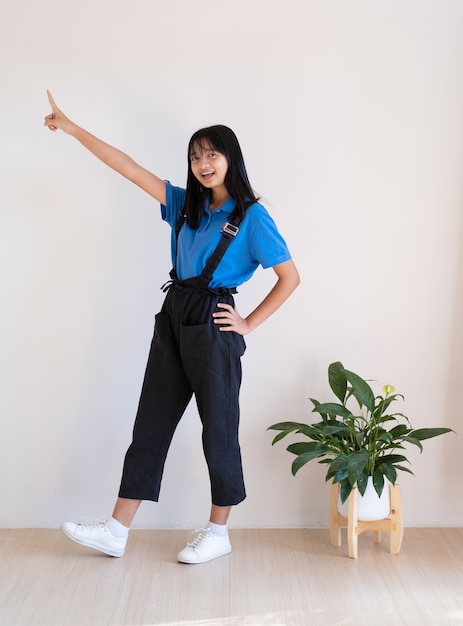 Heureuse jeune fille debout sur le plancher de bois avec une plante verte dans une pièce minimale