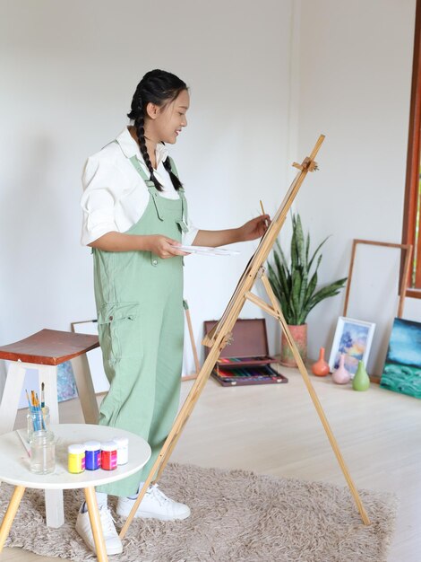 Heureuse jeune fille dessinant avec une palette de peinture et un pinceau chez un artiste peintre à domicile