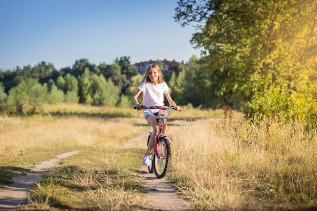 Heureuse jeune fille faisant du vélo dans le pré au jour ensoleillé