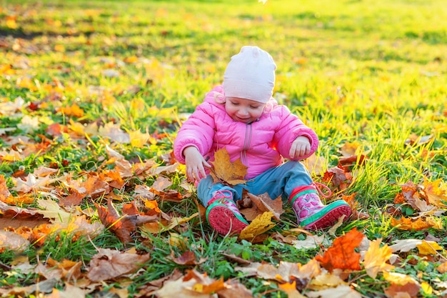 Heureuse jeune fille jouant sous les feuilles jaunes qui tombent dans le magnifique parc d'automne sur la nature se promène en plein air