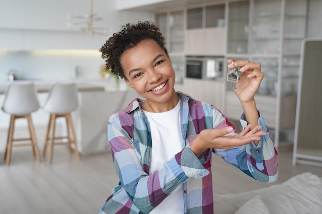 Heureuse jeune fille métisse montrant les clés de la maison à la caméra déplacée dans un nouvel appartement Service immobilier