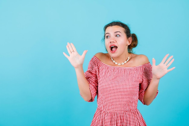 Heureuse jeune fille regarde ailleurs en levant ses poignées sur fond bleu