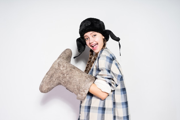 Heureuse jeune fille russe au chapeau de fourrure en attente d'hiver, tenant des bottes en feutre gris