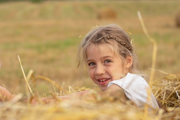 heureuse jeune fille s'asseoir dans la paille sur le terrain agricole
