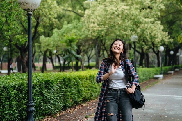 heureuse jeune fille avec sac à dos après l'école rentrant à la maison en marchant dans le parc sur le chemin de la route mains souriantes joyeuses toucher brosse cheveux doux. Belle femme en riant attrayant se détendre en plein air journée ensoleillée