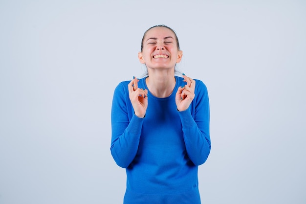 Heureuse jeune fille se tient la main sur la poitrine en croisant les doigts sur fond blanc