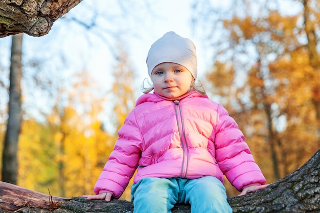 Heureuse jeune fille souriante et assise sur un arbre dans le magnifique parc d'automne sur la nature se promène à l'extérieur Petit enfant jouant en automne automne fond jaune orange Bonjour concept d'automne