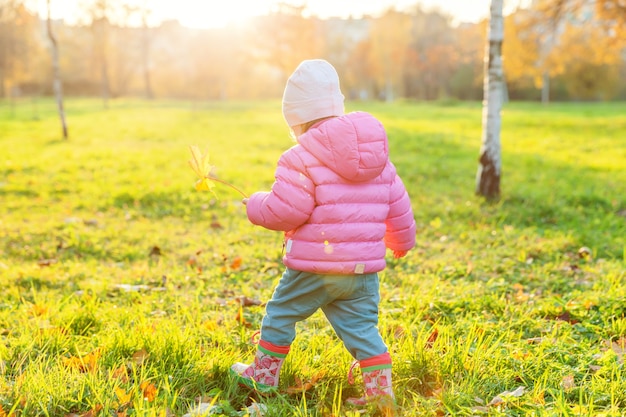 Heureuse jeune fille souriante dans le magnifique parc d'automne sur la nature se promène à l'extérieur. Petit enfant jouant avec la chute de la feuille d'érable jaune en automne automne fond jaune orange. Bonjour concept d'automne.