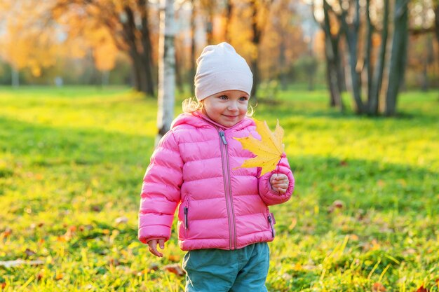 Heureuse jeune fille souriante dans le magnifique parc d'automne sur la nature se promène à l'extérieur. Petit enfant jouant avec la chute de la feuille d'érable jaune en automne automne fond jaune orange. Bonjour concept d'automne.