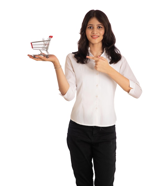 Heureuse jeune fille souriante avec un panier de chariot miniature sur fond blanc Belle fille dans le concept de shopping