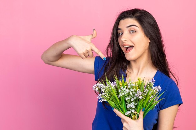 Heureuse jeune fille tenant un bouquet de fleurs et pointant le doigt vers eux