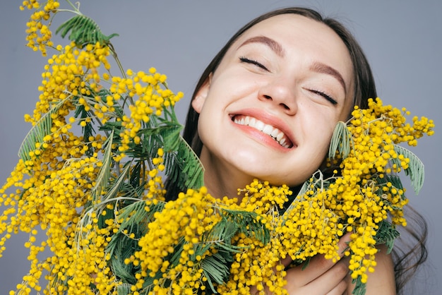 Heureuse jeune fille tenant un gros bouquet d'un mimosa jaune parfumé, souriant et profitant du printemps