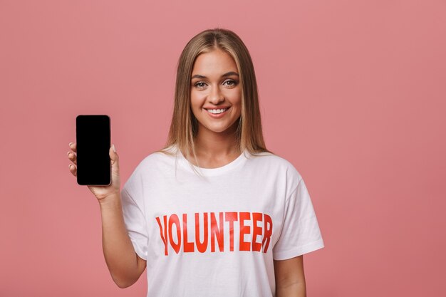 Heureuse jeune fille volontaire isolée, montrant un téléphone portable à écran blanc