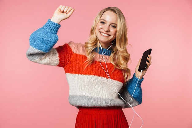 heureuse jeune jolie belle femme posant isolée sur un mur rose à l'aide d'un téléphone portable écoutant de la musique avec des écouteurs