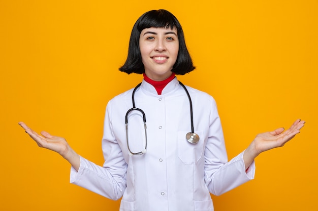 Heureuse jeune jolie femme caucasienne en uniforme de médecin avec stéthoscope gardant les mains ouvertes