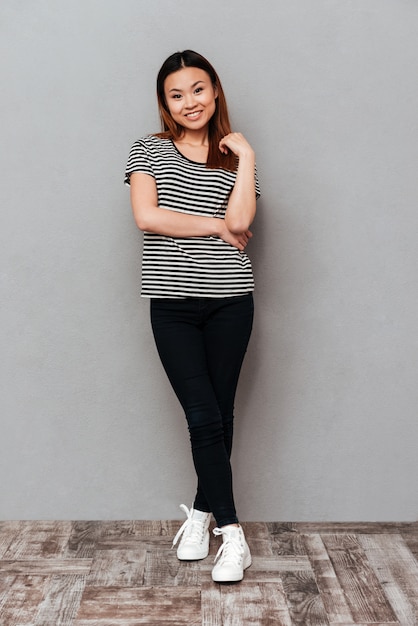 Heureuse jeune jolie femme debout sur un mur gris.