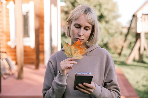 Heureuse jeune jolie femme marchant à l'extérieur dans le parc d'automne à l'aide de chat de téléphone portable