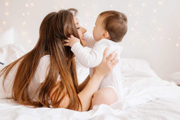 Heureuse jeune maman embrasse bébé dans son lit