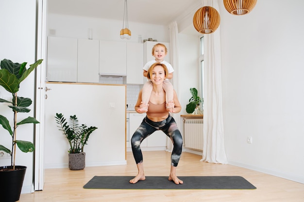 Heureuse jeune maman faisant des squats avec son fils tout-petit assis sur son épaule