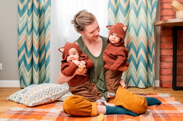 Heureuse jeune maman jouant avec des jumeaux enfants assis sur une couverture à la maison