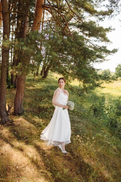 Heureuse jeune mariée dans une robe de mariée blanche de forêt de pins