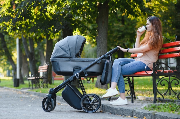 Heureuse jeune mère avec bébé en buggy assis sur un banc dans le parc en automne