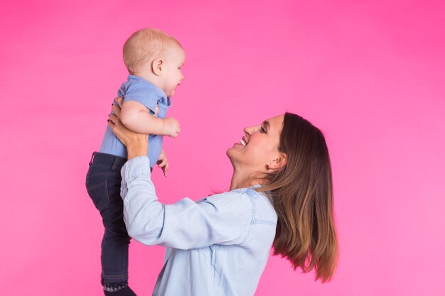 Heureuse jeune mère avec un bébé enfant sur un mur rose.