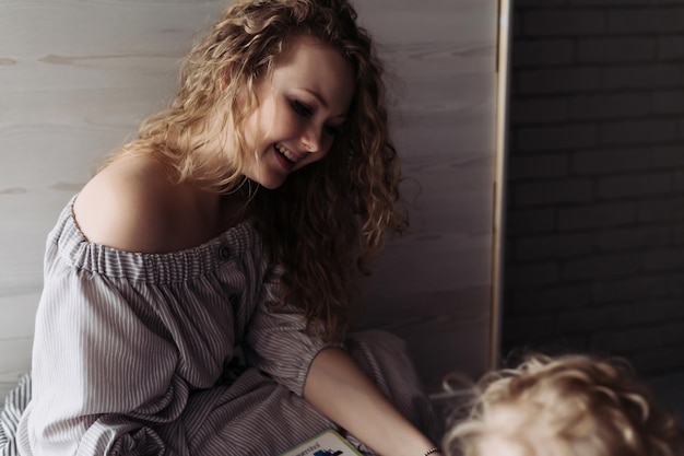 Heureuse jeune mère bouclée vêtue d'une robe jouant avec son petit fils, riant, s'amusant