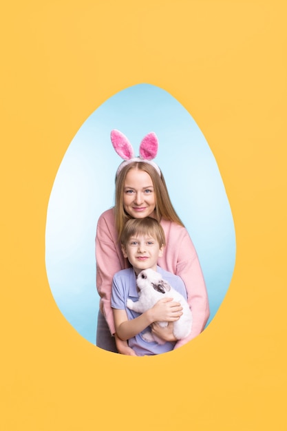 Heureuse jeune mère embrassant son fils avec lapin mignon tout en posant dans le cadre de l'oeuf de Pâques