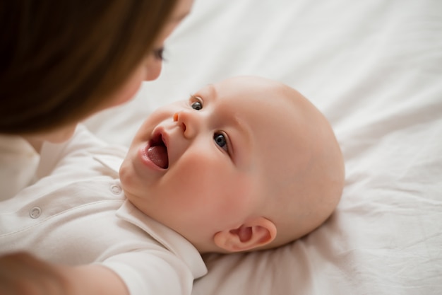 Heureuse jeune mère embrasse bébé à la maison sur le lit