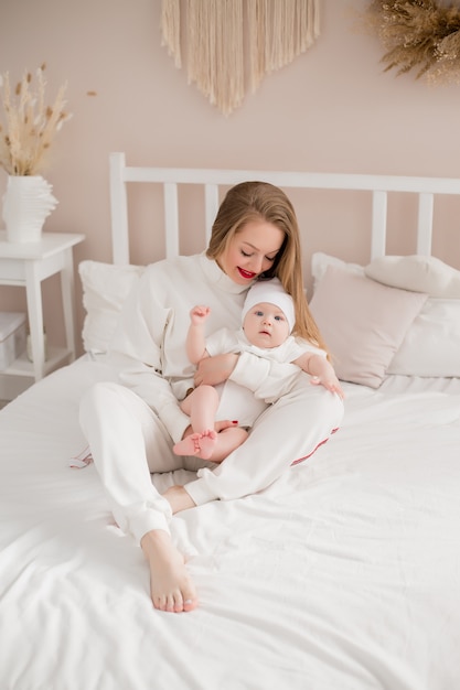 Heureuse jeune mère embrasse bébé à la maison sur le lit