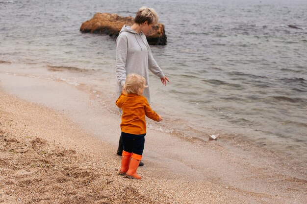 Heureuse jeune mère jouant avec un bateau en papier avec son fils par une journée ensoleillée près de la mer Repos sur la plage Une famille heureuse