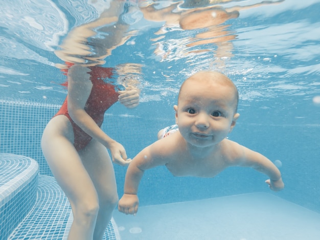 Photo heureuse jeune mère jouant avec son bébé dans la piscine extérieure par une chaude journée d'été. tir sous-marin