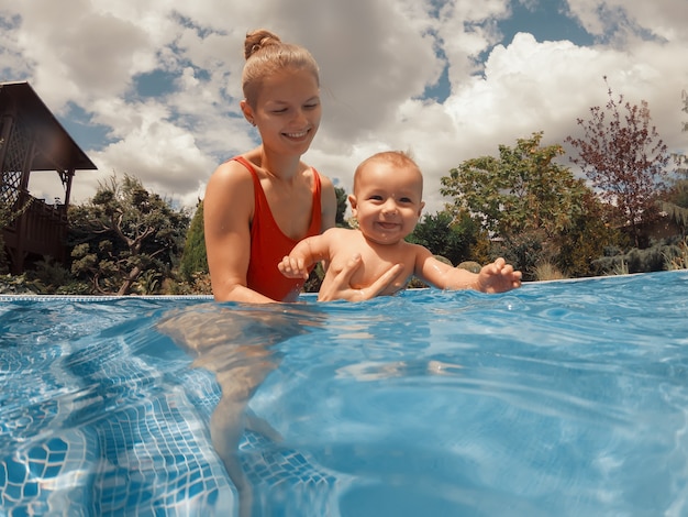 Heureuse jeune mère jouant avec son bébé dans la piscine extérieure par une chaude journée d'été