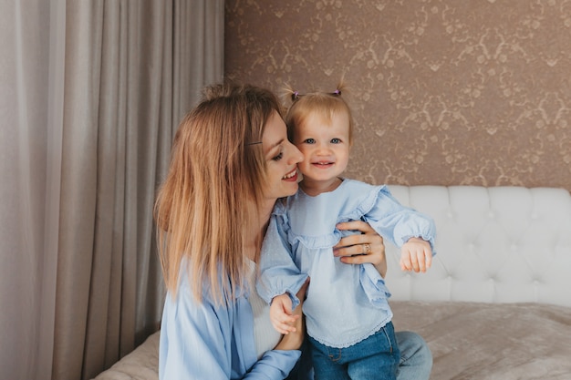 Heureuse jeune mère joue avec sa fille sur le lit à la maison. fête des mères.