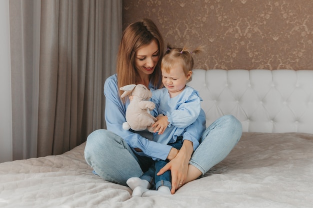 Heureuse jeune mère joue avec sa fille sur le lit à la maison. fête des mères.