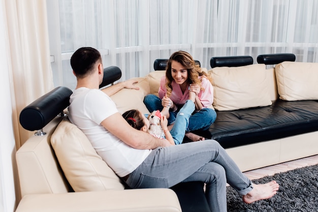 Heureuse jeune mère et père avec petite fille assise sur le canapé,