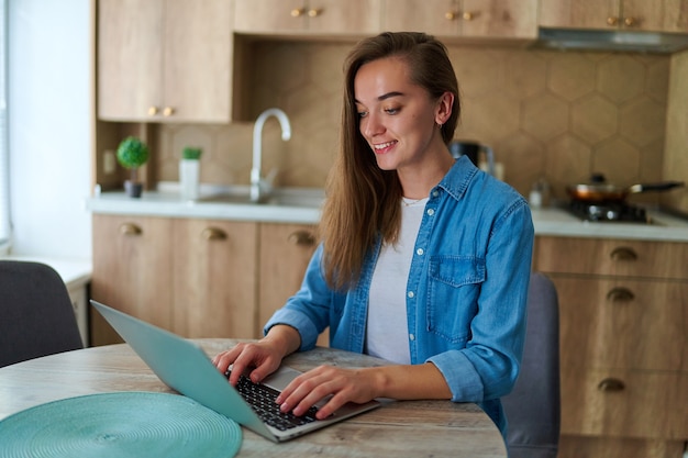 Heureuse jeune pigiste intelligente du millénaire à succès travaillant en ligne sur un ordinateur portable à distance à la maison. Utilisation d'un ordinateur pour taper, discuter, naviguer et créer des réseaux sociaux