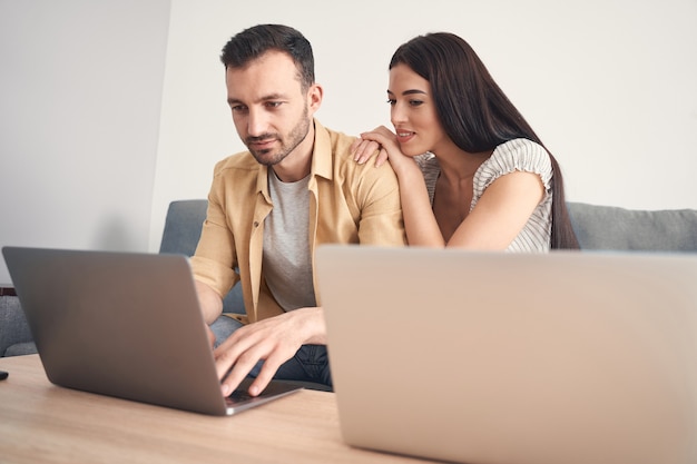 Heureuse jolie femme assise sur un canapé près de son homme bien-aimé et mettant les mains sur son épaule