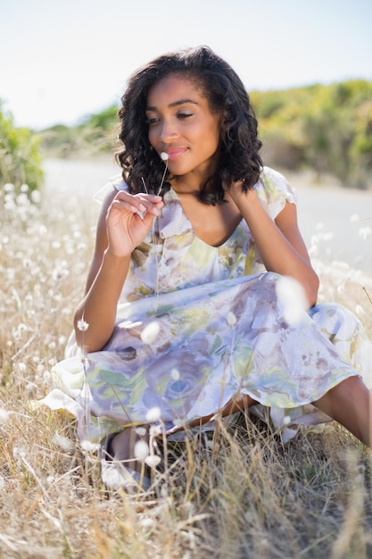 Heureuse jolie femme assise sur l&#39;herbe en robe fleurie