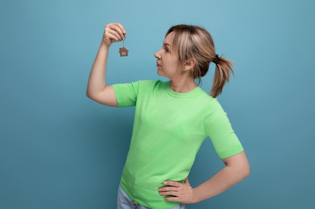 Heureuse jolie femme blonde au look décontracté tenant un nouveau trousseau d'appartement sur fond bleu