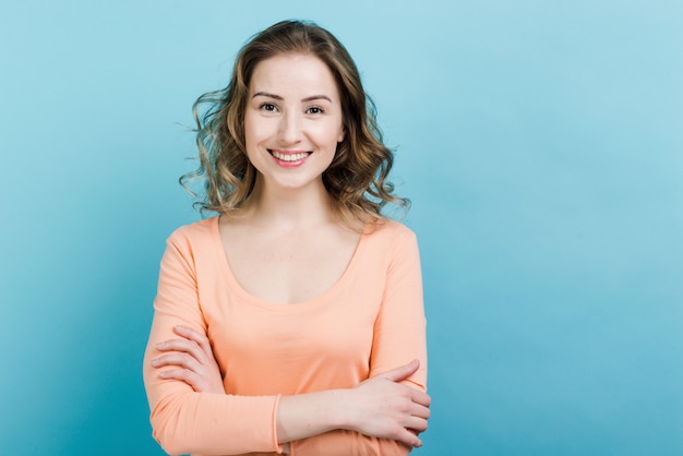 Heureuse jolie femme debout avec les mains jointes portant des vêtements décontractés sur le mur bleu