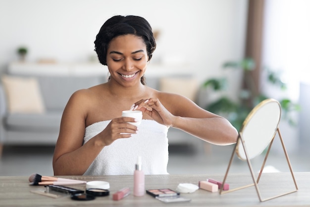 Photo heureuse jolie femme noire à l'aide de crème pour le visage