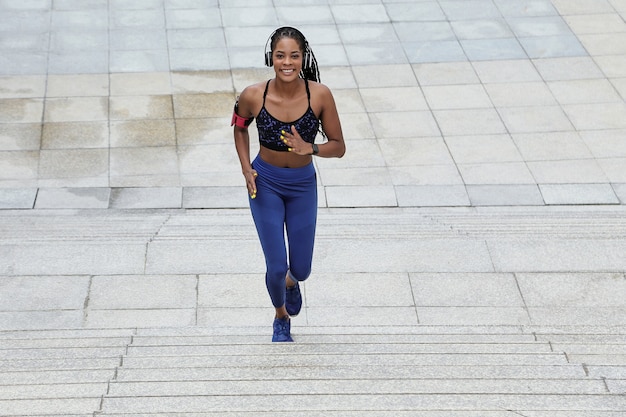 Heureuse jolie femme noire jogger en haut et leggins qui monte les escaliers et regardant la caméra