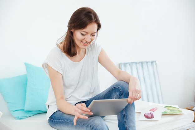 Heureuse jolie femme peintre avec tablette assis dans un studio d'art