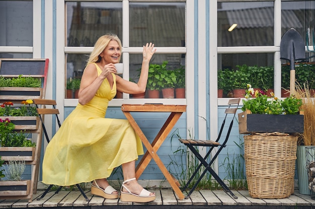 Heureuse jolie femme vêtue d'une robe d'été légère et de sandales compensées à la mode, assise à une table