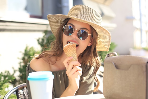 Heureuse jolie fille mangeant une glace tout en étant assise au café de la rue d'été.