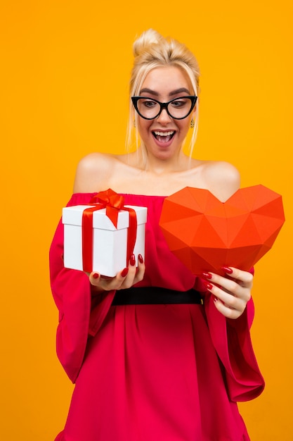 Heureuse jolie fille tend une boîte-cadeau sur le mur jaune